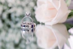 a diamond ring sitting on top of a table next to a white rose