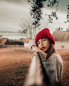 a woman wearing a red hat leaning on a fence