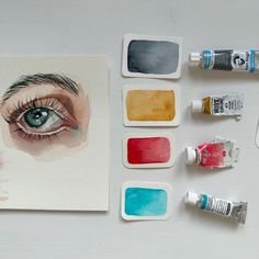 some watercolors are sitting on a table next to an eye