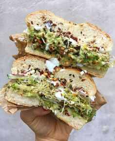 two halves of a sandwich with lettuce and other toppings on it in someone's hand