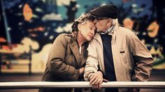 an older man and woman are kissing on a rail outside in the city at night