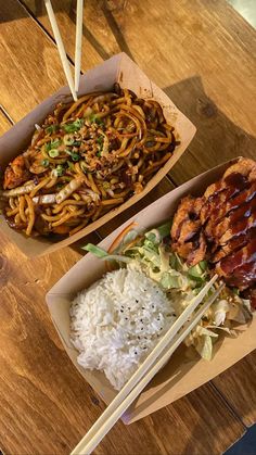 two boxes filled with food sitting on top of a wooden table next to chopsticks