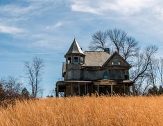 an old house sitting on top of a dry grass covered hill in front of trees