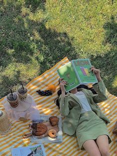 a woman laying on top of a yellow and white checkered blanket next to an open book