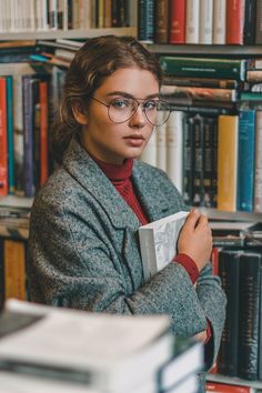 a woman with glasses is holding a book in front of a bookshelf full of books