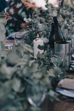 the table is set with silverware, candles and greenery for an elegant dinner