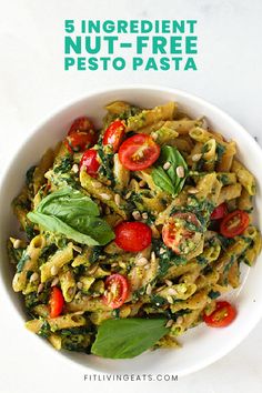 a white bowl filled with pesto pasta and topped with tomatoes, spinach and basil