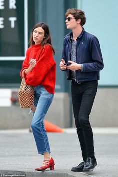 a young man and woman walking down the street together, one holding a handbag