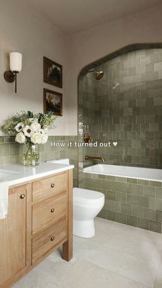 a bathroom with green tiles and white flowers in the vase on the sink counter next to the bathtub