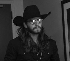 a man with long hair wearing a cowboy hat and glasses is looking at the camera