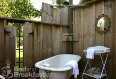 an old fashioned bathtub and sink in a wooden fenced outdoor area with white towels on the rack