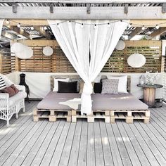 an image of a wooden patio with white drapes and pillows on the couches