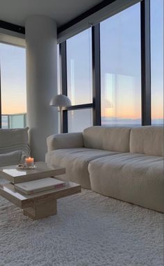 a living room filled with white furniture and large windows overlooking the ocean at sunset or dawn