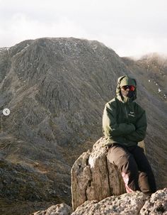 a man sitting on top of a large rock next to a lush green mountain range