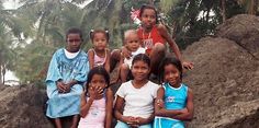 a group of children sitting on top of a pile of rocks next to palm trees