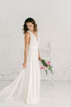 a woman in a white wedding dress holding a bouquet and looking down at the floor