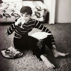 a woman sitting on the floor eating food from a plate while holding a book in her hand