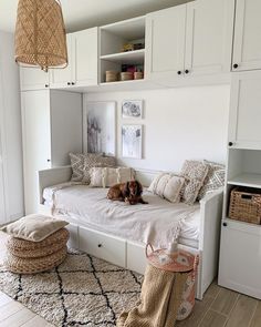 a dog laying on top of a bed in a room with white cabinets and drawers