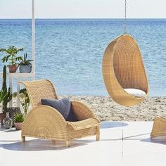 two hanging chairs on the beach next to an umbrella and potted plants in front of the ocean