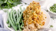 a white plate topped with green beans and meat covered in sauce next to some parsley