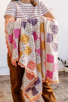 a woman is holding up a crocheted blanket