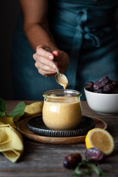 a woman is spooning something out of a jar with lemons and raisins in the background