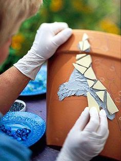 a person in white gloves is working on a clay pot with paint and paper over it