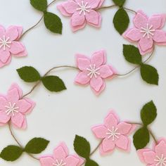 pink felt flowers and green leaves on a white surface