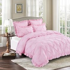 a bed with pink comforter and pillows in a room next to a window,