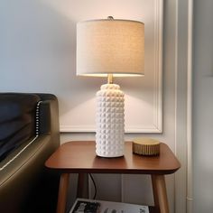 a white lamp sitting on top of a wooden table next to a black leather couch