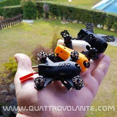 a hand holding four small toy cars in front of a swimming pool and lawn area