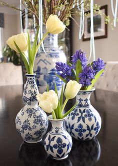 three blue and white vases with tulips in them on a black table