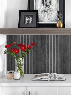 some red flowers are in a vase on a white table with a black and white wall behind it