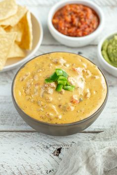 a bowl filled with dip surrounded by bowls of salsa and tortilla chips