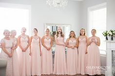 a group of women standing next to each other in front of a fireplace wearing pink dresses