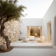 an outdoor living area with white furniture and a tree in the corner, next to a stone wall