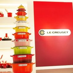 a stack of red and green pots sitting on top of each other in front of a le creuset sign