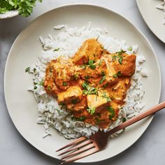 a white plate topped with rice and chicken next to a fork on top of a table