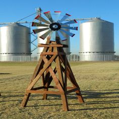 a wooden windmill sitting in the middle of a field next to two silo's