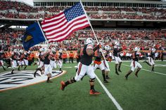 the football team is running on to the field with an american flag in their hand