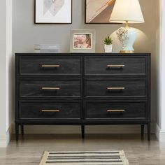 a black dresser with two pictures on the wall above it and a rug in front of it