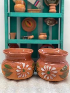 two brown vases sitting on top of a counter next to a shelf with dishes