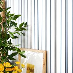 yellow flowers are in a vase next to a picture frame on a shelf with a striped wallpaper behind it