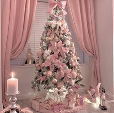 a decorated christmas tree in front of a window with pink curtains and presents under it