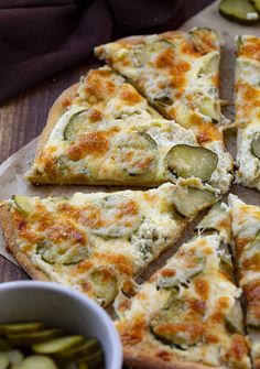 a sliced pizza with zucchini and cheese on it next to a bowl of pickles