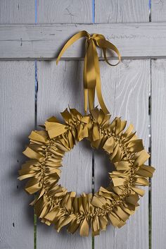 a gold wreath hanging on the side of a white wooden wall with a yellow ribbon