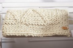 a white knitted blanket sitting on top of a wooden bench next to a wall