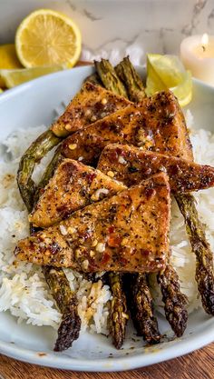 a white plate topped with rice and asparagus covered in seasoning next to lemon wedges