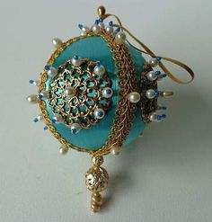 a close up of a brooch on a white surface with blue beads and gold chains