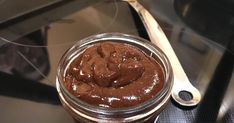 a jar filled with chocolate frosting next to a spoon on top of a stove